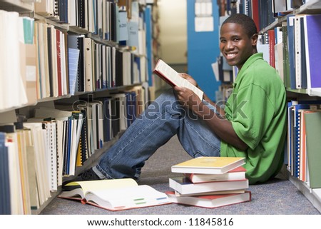 Male university student sitting on library floor surrounded by books