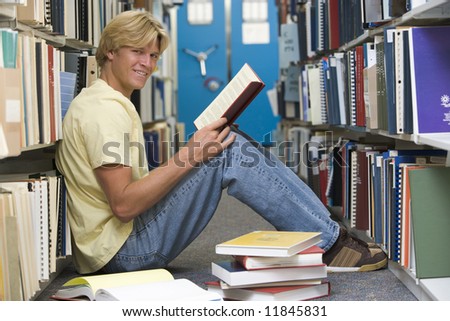 Male university student sitting on floor surrounded by books