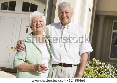 Senior couple standing outside front door of home