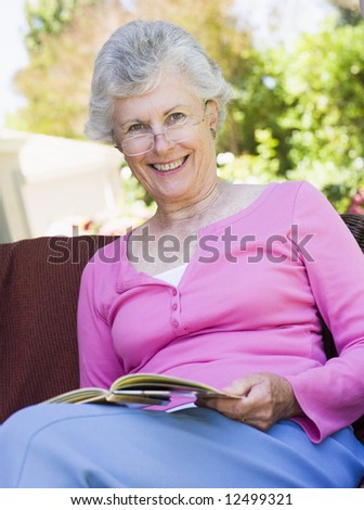 Senior woman reading book outside looking to camera