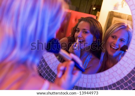 Two young women applying makeup in a nightclub bathroom