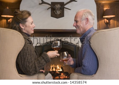 Couple sitting in living room by fireplace with drinks smiling