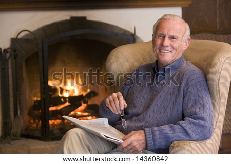 Man sitting in living room by fireplace with newspaper smiling