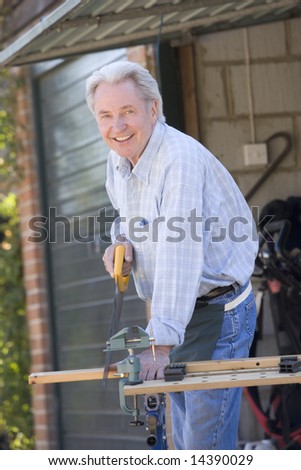 Man at shed sawing wood and smiling