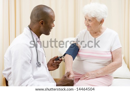 Doctor checking woman\'s blood pressure in exam room smiling