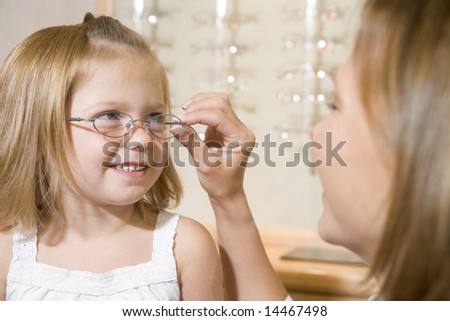 Woman trying eyeglasses on young girl at optometrists smiling
