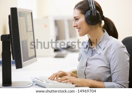 stock photo Woman wearing headphones in computer room typing and smiling
