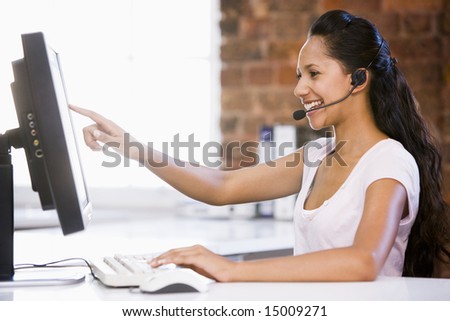 Businesswoman in office wearing headset and pointing at computer monitor