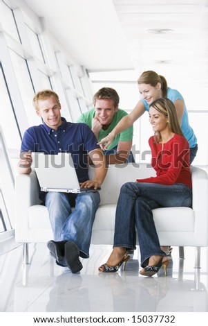 Four people in lobby pointing at laptop smiling