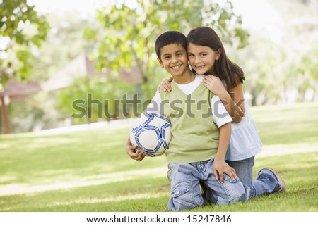 Two children playing football in park looking to camera