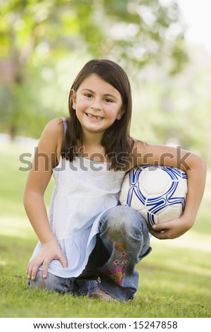 Girl in park holding football looking to  camera