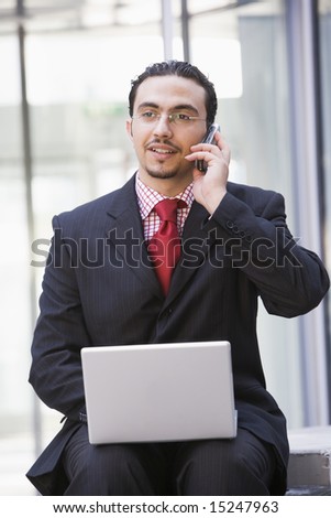 Businessman using laptop and mobile phone outside office