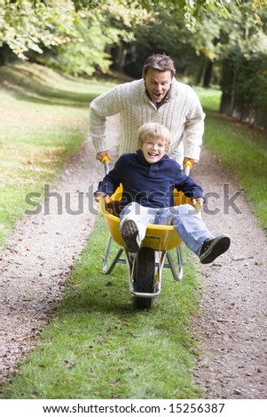 Father giving son ride in wheelbarrow through autumn woods