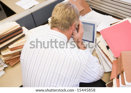 Businessman in cubicle with laptop and stacks of files