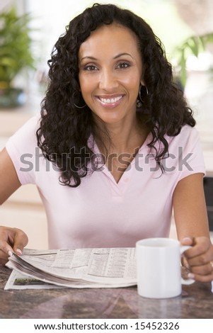 Woman in kitchen with newspaper and coffee smiling