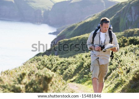 Man walking on cliffside path looking at map
