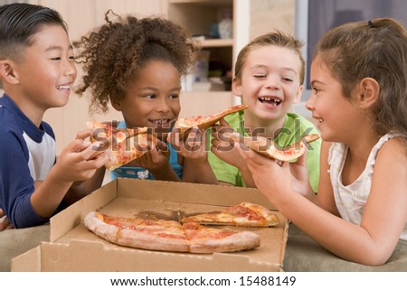 Four young children indoors eating pizza smiling