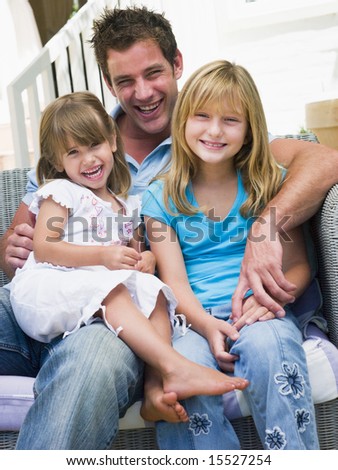 Man and two young girls sitting on patio smiling