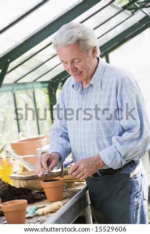 Man in greenhouse putting seed in pot smiling
