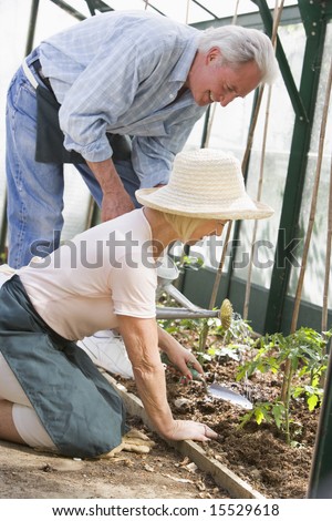 Woman in greenhouse planting seeds and man holding watering can smiling
