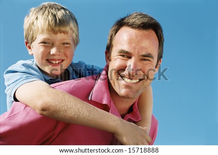 Father giving son piggyback ride outdoors smiling