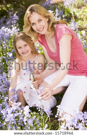 Mother and daughter outdoors holding flowers smiling