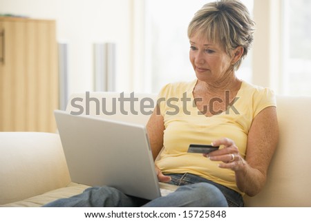 Woman in living room with laptop and credit card smiling