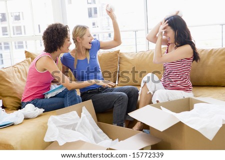 Three girl friends playfully unpacking boxes in new home smiling