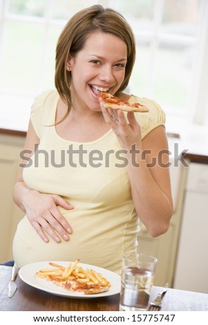 Pregnant woman in kitchen eating French fries and pizza smiling