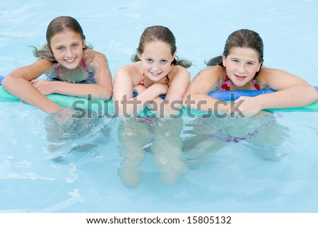 Three young girl friends in swimming pool with pool noodle smiling