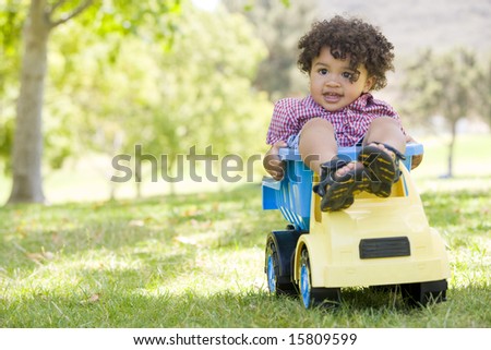 Young boy outdoors playing on toy dump truck smiling