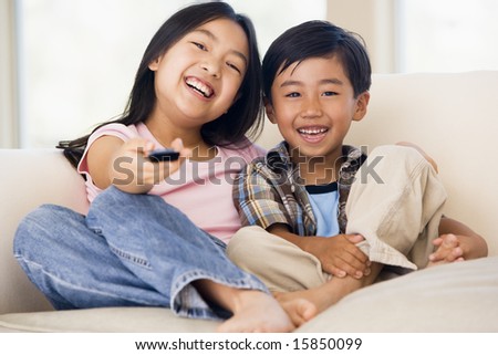 Two young children in living room with remote control smiling