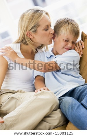 Woman kissing disgusted young boy in living room
