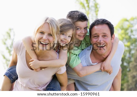 Couple giving two young children piggyback rides smiling Couple giving two young children piggyback rides smiling