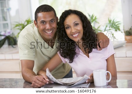 Couple in kitchen with newspaper and coffee smiling