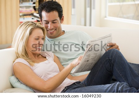 Couple in living room reading newspaper and smiling
