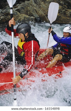 Two people paddling inflatable boat down rapids