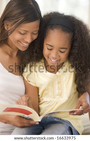 Woman and young girl sitting in living room reading book and smiling