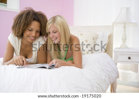 Teenage Girls Lying On Bed Reading Together