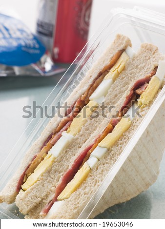Egg And Bacon Sandwich On White Bread With A Bag Of Crisps And A Can Of Fizzy Drink