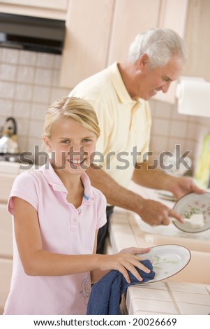 Grandfather And Granddaughter Cleaning Dishes Together