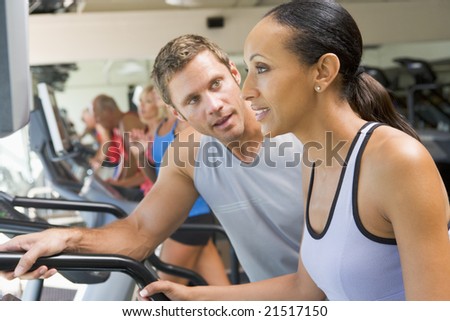 Personal Trainer Encouraging Woman Using Treadmill At Gym