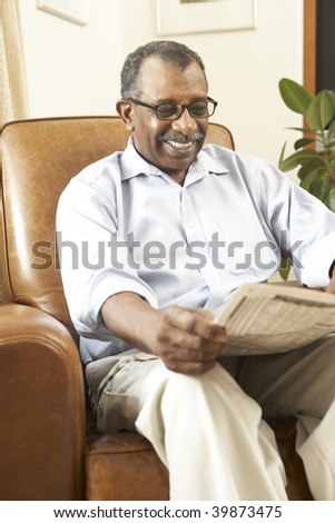 Senior Man Sitting In Armchair Reading Newspaper