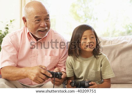 Grandfather And Granddaughter Playing Computer Game At Home