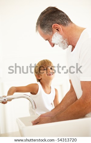 Grandson Watching Grandfather Shaving In Bathroom Mirror