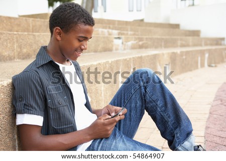 Male Teenage Student Sitting Outside On College Steps Using Mobile Phone