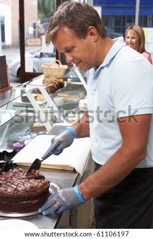 Man Working Behind Counter In Cafe Slicing Cake