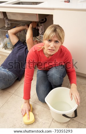 Woman Mopping Up Leaking Sink Whilst Plumber Works