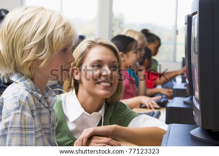 Teacher helping student at computer terminal with students in background (depth of field/high key)