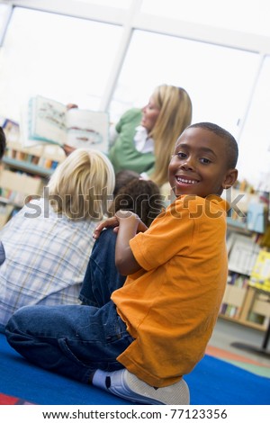 Student in class looking at camera with teacher reading in background (selective focus)